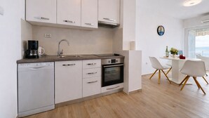 Cozinha moderna com armários brancos, lava-louças, cafeteira e forno. Há uma área de jantar com mesa e cadeiras brancas.