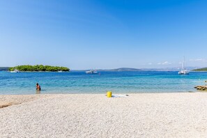 Une plage de galets avec des bateaux et une île au loin.