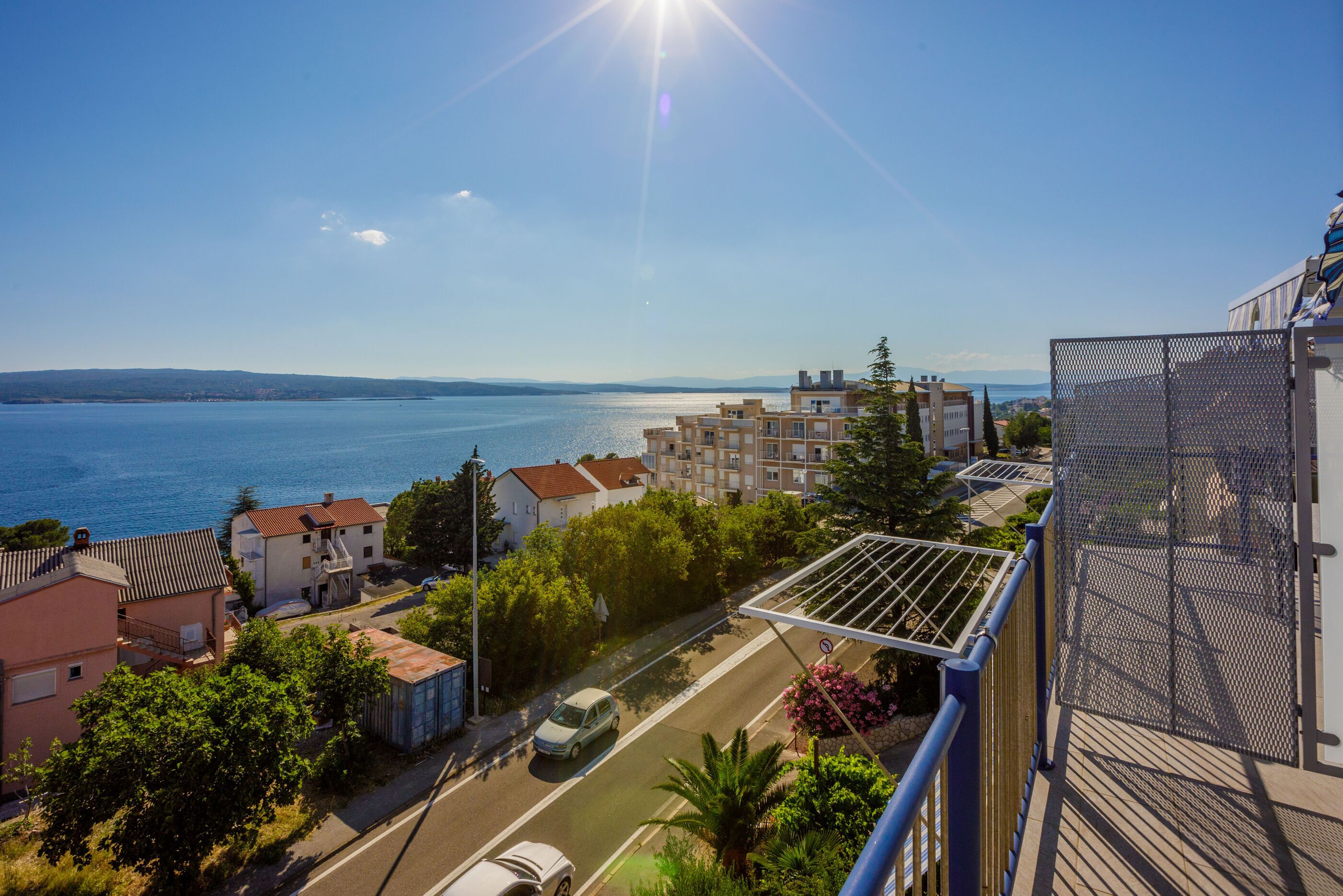 Una zona residencial costera con vista despejada al mar, una calle con un coche aparcado y edificios con balcones.