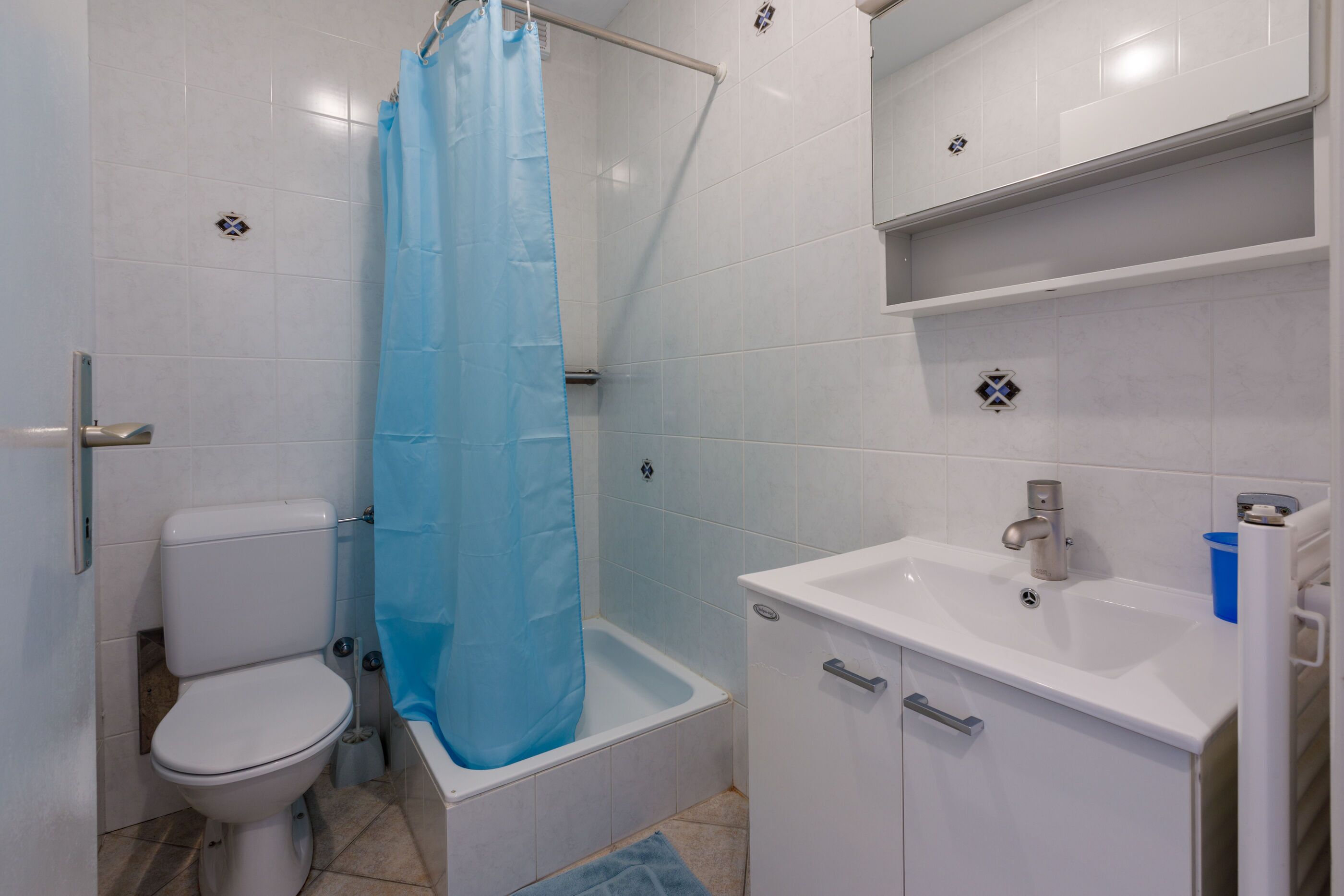 A bathroom with a toilet, a bathtub with a shower curtain, a sink, and a cabinet.