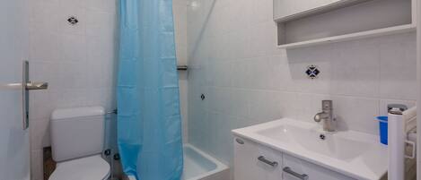 A bathroom with a toilet, a bathtub with a shower curtain, a sink, and a cabinet.