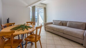 Un comedor con una mesa redonda de madera y sillas, un sofá color beige y vistas al exterior a través de una puerta corrediza de vidrio.