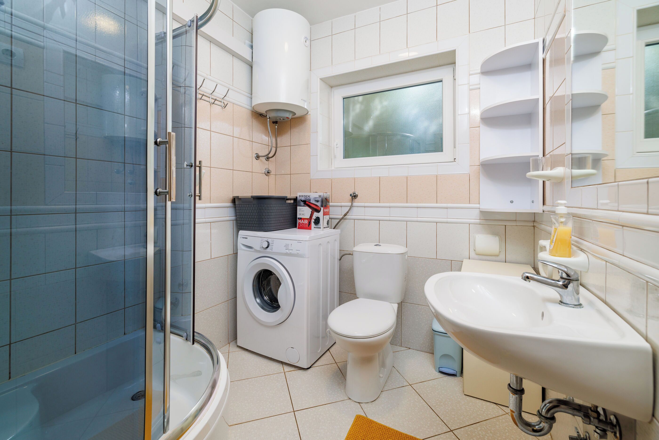 A modern bathroom with a glass shower enclosure, a washing machine, a toilet, and a sink with a mirror.