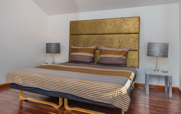 Ein Schlafzimmer mit einem großen Bett, zwei Nachttischlampen und einem Kopfteil mit einer strukturierten Oberfläche.