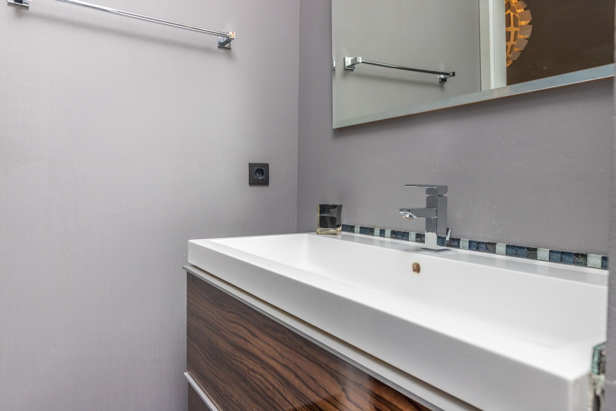 Un baño con lavamanos blanco, un espejo y un perchero para toallas.