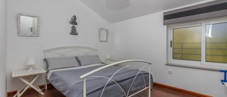 Un dormitorio con cama, mesita de noche, lámpara, decoración en la pared y ventana con persianas.