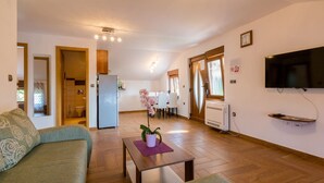 A living room with a sofa, a coffee table with a plant, a TV mounted on the wall, and a kitchen in the background. - Apartments Sobol (Crikvenica)