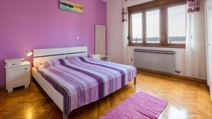 A bedroom with a bed, a nightstand, a lamp, a window with curtains, and a radiator. - Apartments Sobol (Crikvenica)