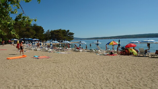 A beach with rows of sun loungers and umbrellas, a clear sky, and a calm sea. - Apartments Sobol (Crikvenica)