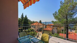 A balcony with a glass table and chairs, overlooking a coastal area with red-roofed buildings and a clear blue sky. - Apartments Sobol (Crikvenica)