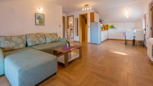 A living room with a sofa, a coffee table, and a kitchen area with a refrigerator and dining table. - Apartments Sobol (Crikvenica)