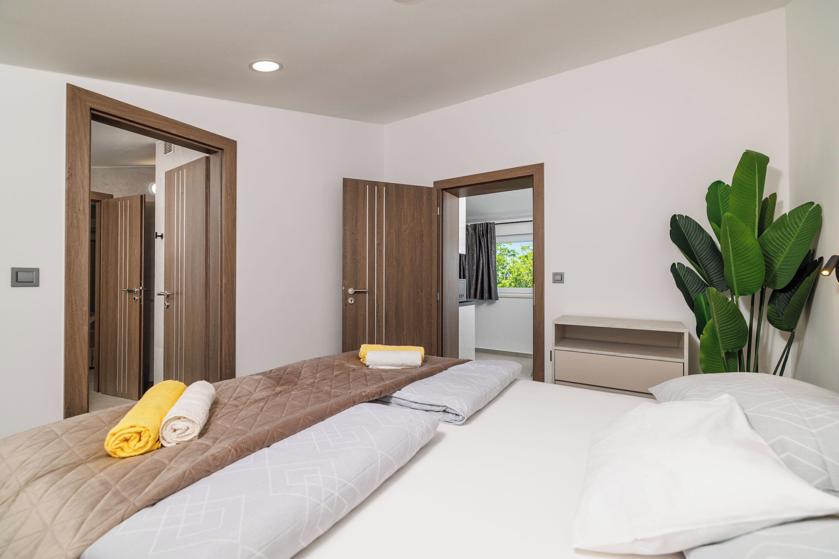 Ein Hotelzimmer mit zwei Betten, einer großen Pflanze im Topf und Blick ins Freie.