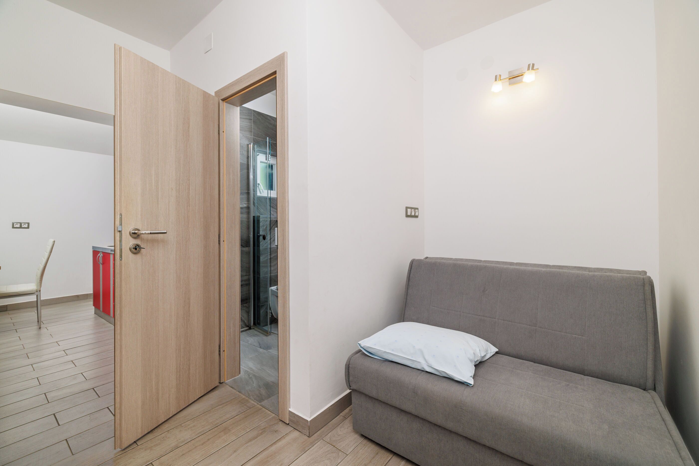 Ein Zimmer mit Holztür, einem grauen Sofa, einem Sessel und einem roten Schrank.