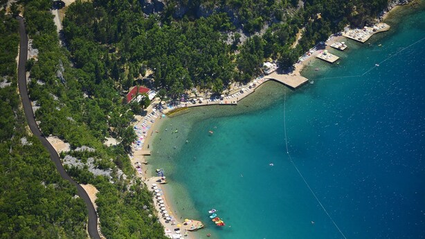 Μια αεροφωτογραφία μιας παράκτιας περιοχής με μια παραλία, έναν δρόμο και μια μικρή προβλήτα.