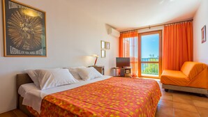 Una habitación de hotel con una cama, televisión, silla y balcón con cortinas naranjas.