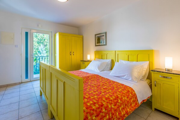 Une pièce avec un lit, des armoires jaunes, une porte donnant sur un balcon et un tableau encadré au mur.