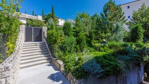 Una escalera de piedra conduce a una entrada vigilada, rodeada de vegetación exuberante y altos árboles.