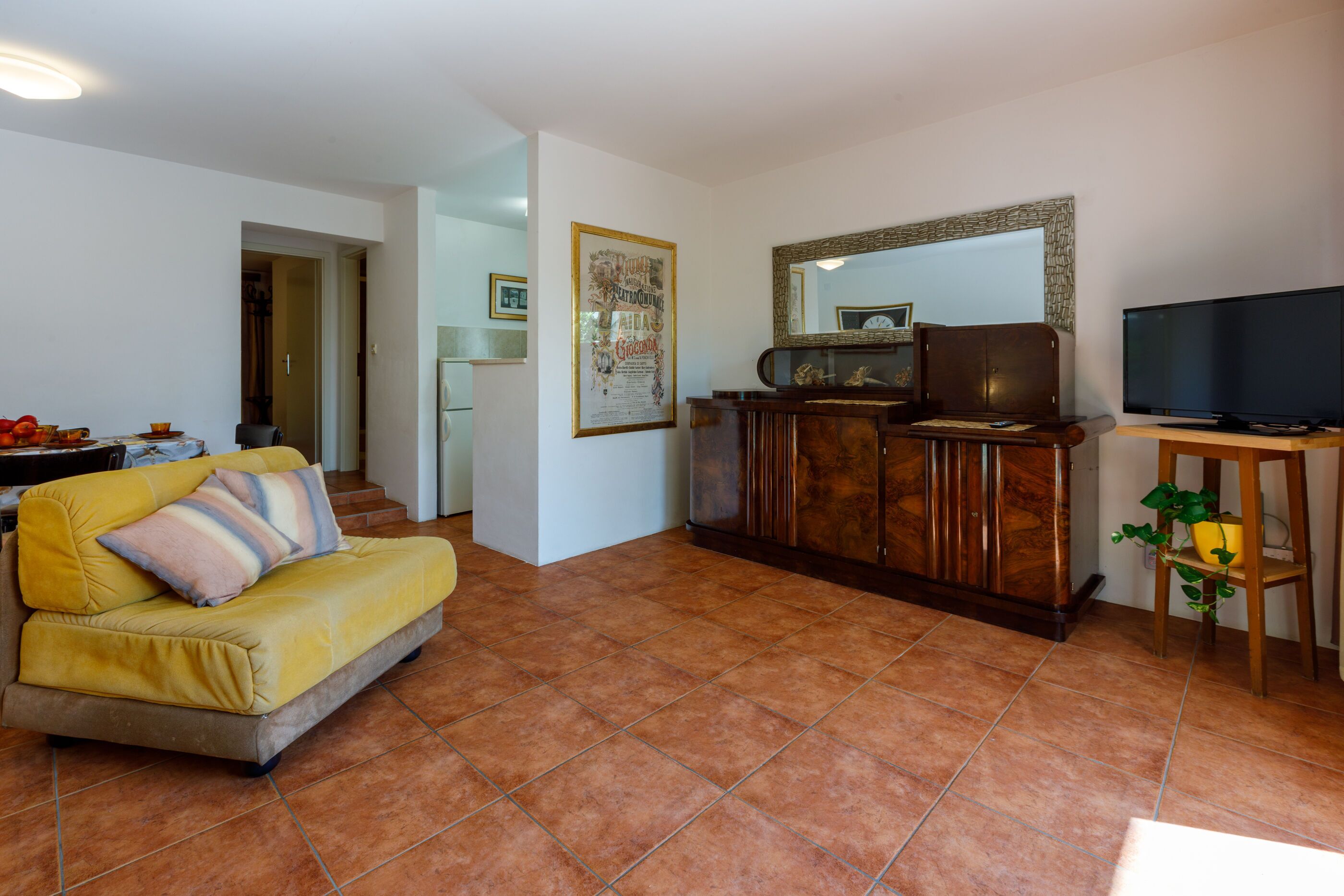 A living room with a yellow sofa, a wooden cabinet, a television, and a mirror.