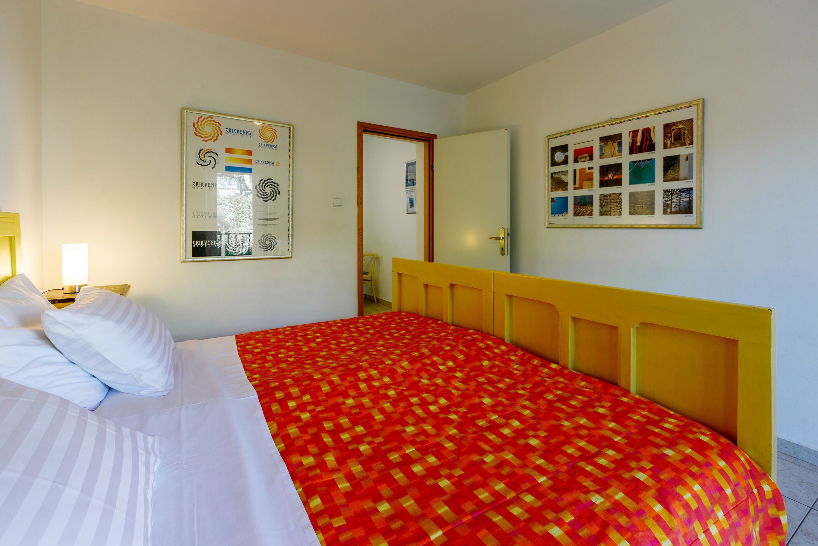 A hotel room with a bed, a nightstand, a wall with framed pictures, and a door.