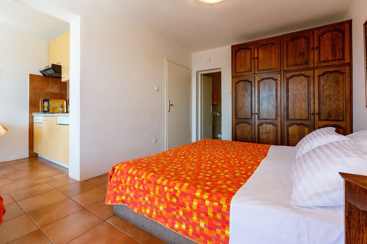 Un dormitorio con cama, armario de madera y una cocina visible a través de una puerta abierta.