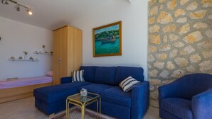 Ein Wohnzimmer mit einem blauen Sofa, einem kleinen Couchtisch, einem Bett mit rosa Bettdecke, einem Holzschrank und einer Steinwand.