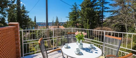 A balcony with a round table, chairs, and a vase of flowers.