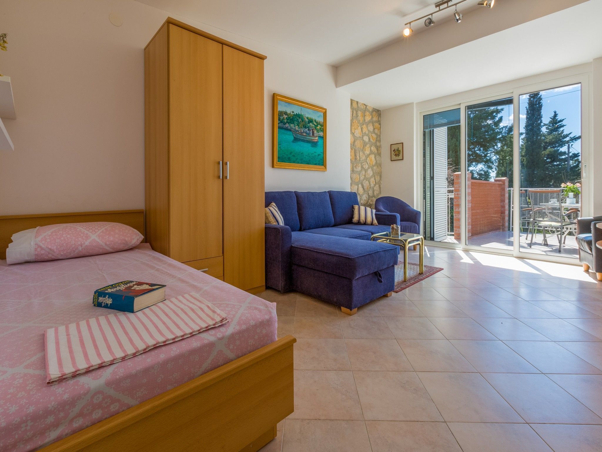 A bedroom with a bed, a wardrobe, a sofa, and a balcony with a table and chairs.