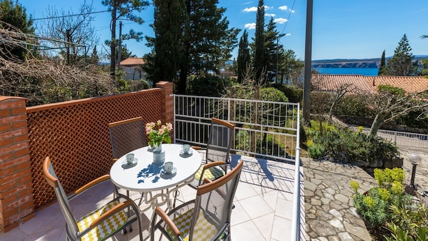 Eine Terrasse mit einem runden Tisch und Stühlen, einer Ziegelwand und Blick auf das Meer.