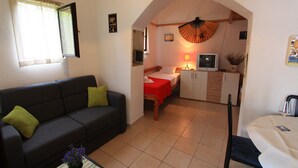 A compact living space with a sofa, a dining table, a kitchenette, and a bed. - Apartment Giardino (Selce)