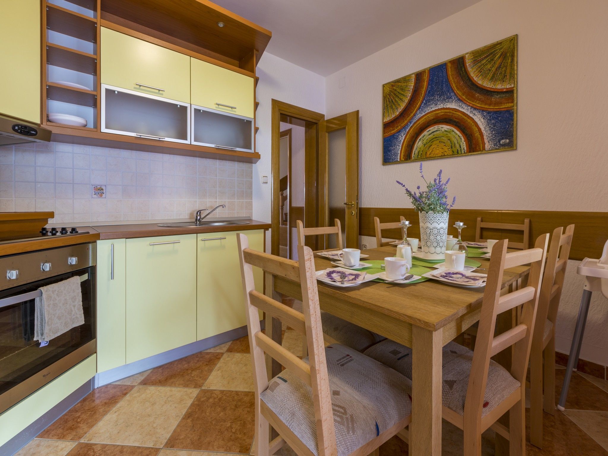 Una cocina con una mesa de comedor lista para cuatro personas, sillas de madera y un cuadro en la pared.