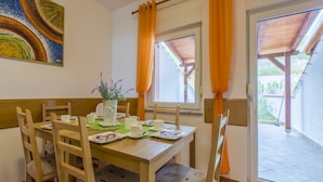 Un comedor con mesa y sillas de madera, un florero con flores y una ventana con cortinas naranjas.
