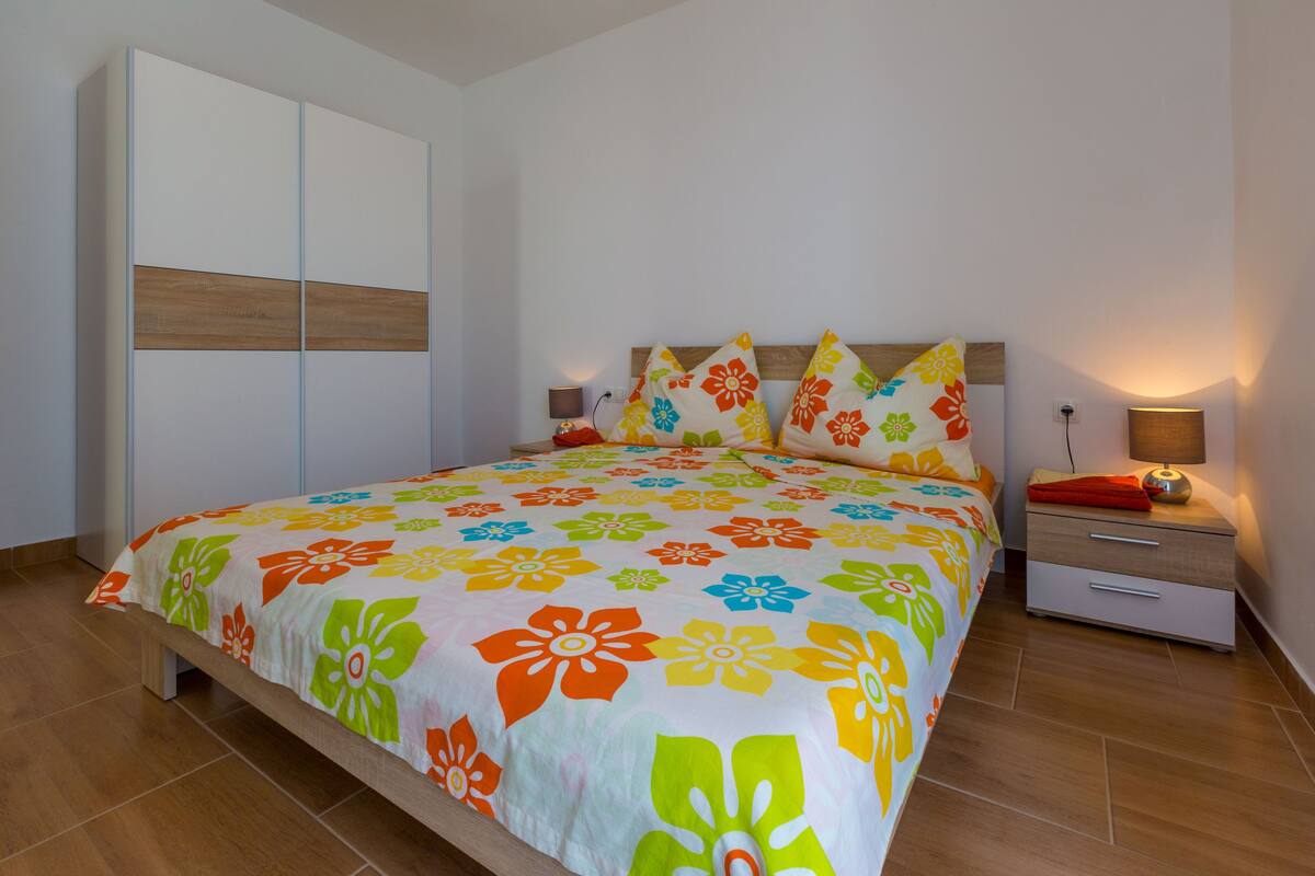 Un dormitorio con cama, mesitas de noche, un armario y una lámpara.