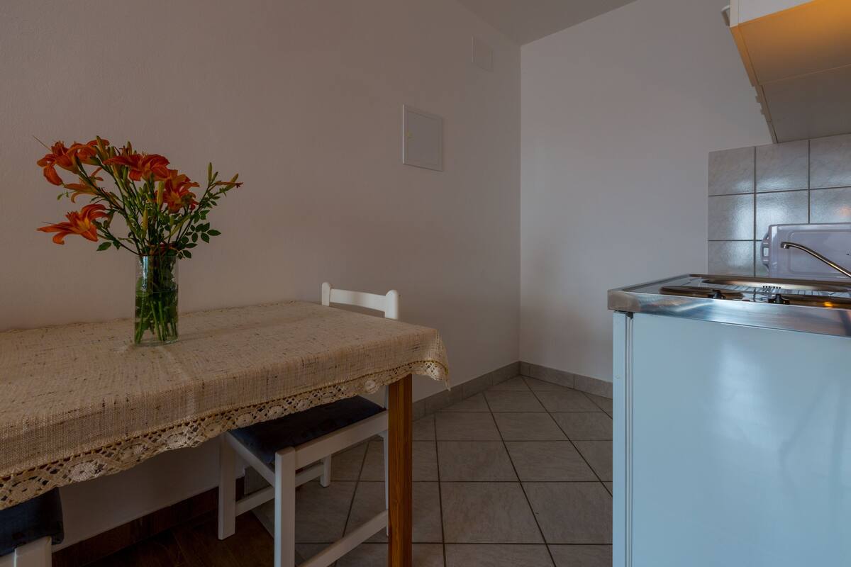 Una cocina con una mesa blanca, un florero con flores y un salpicadero de azulejos.