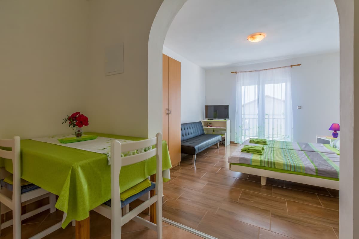 A room with a dining table, a sofa, a TV, and a bed.