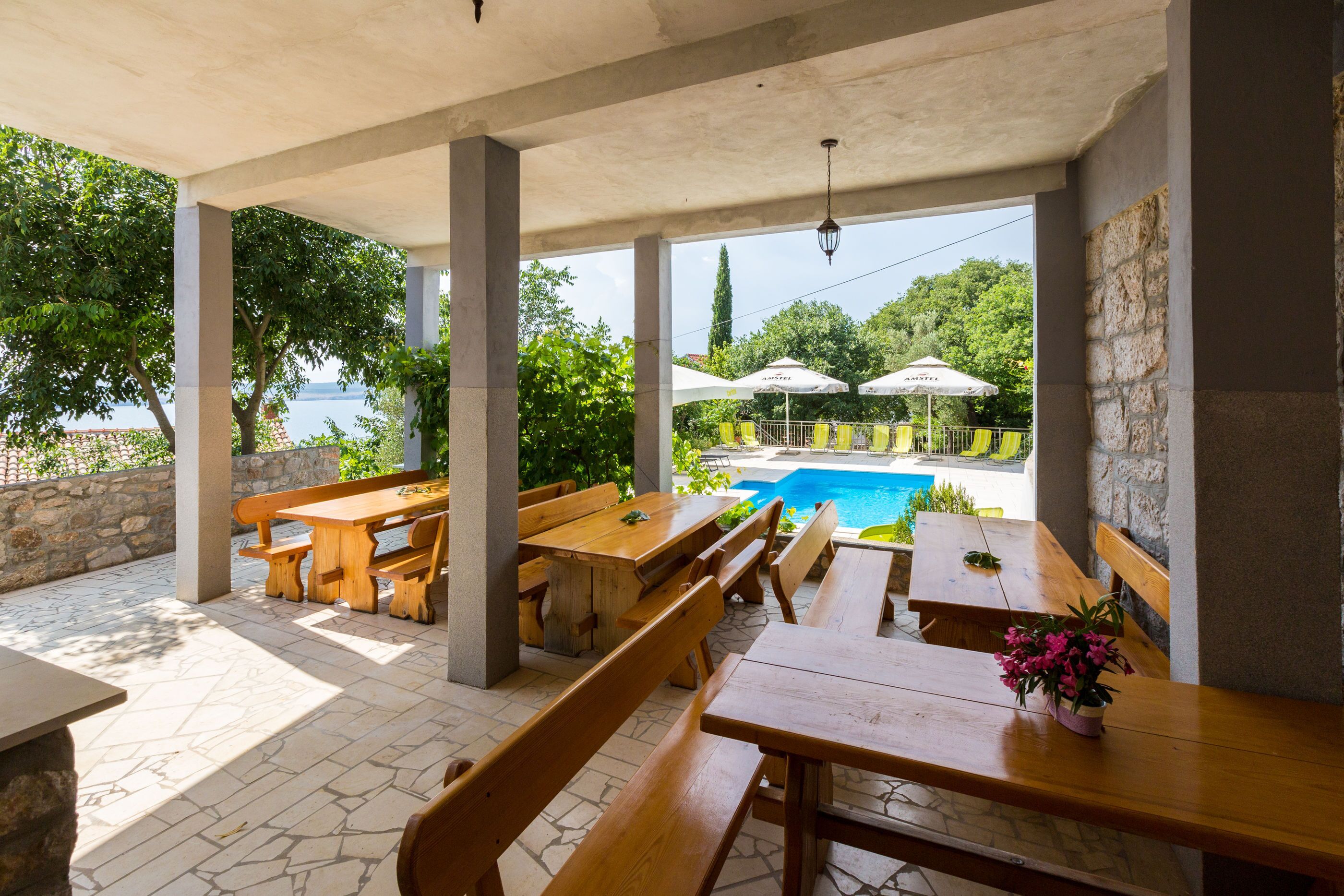 Un espace extérieur aménagé en terrasse, avec des tables et des bancs en bois, une piscine et des parasols.