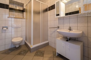 A bathroom with a shower, toilet, sink, and tiled walls.