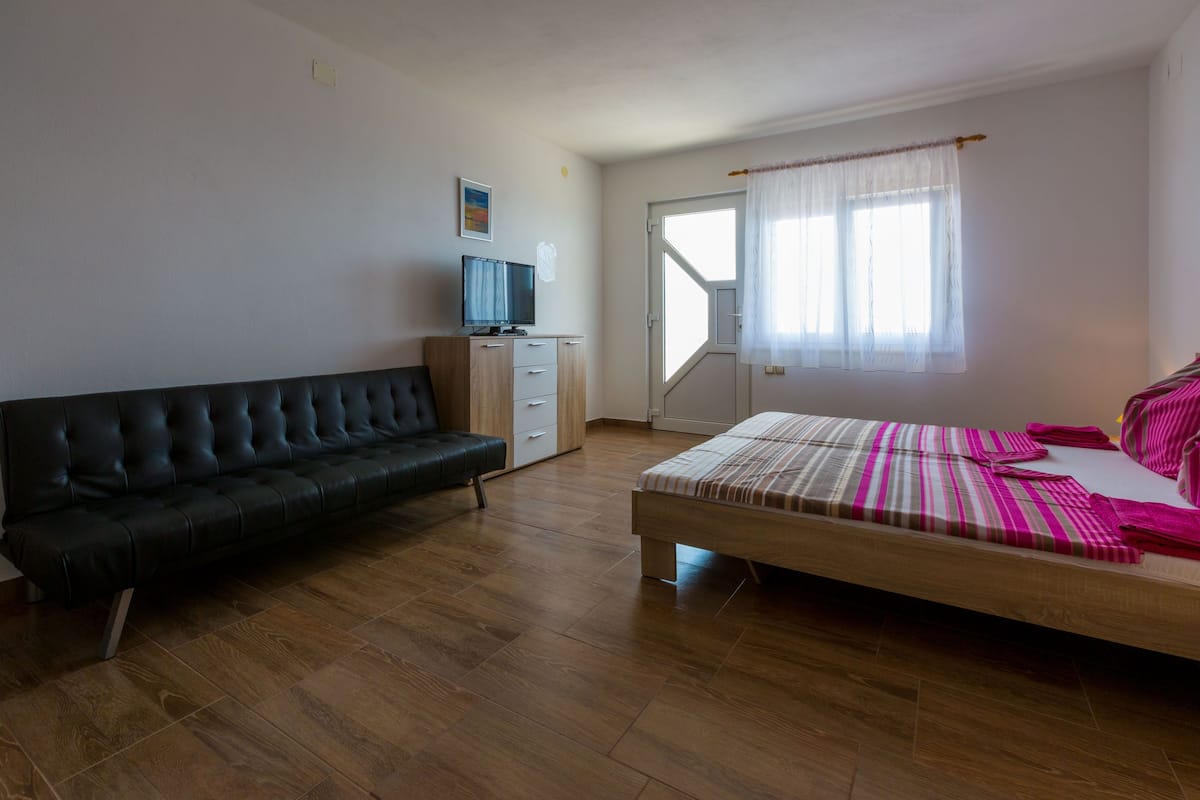 A bedroom with a bed, a black sofa, a TV, and a window with curtains.