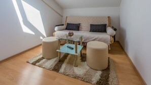 Ein kleiner, gemütlicher Raum mit einer Couch, zwei Hocker, einem Glastisch und einem Teppich.