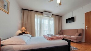 A hotel room with a bed, a sofa, a TV, and a window with curtains. - Apartments Marija (Selce)