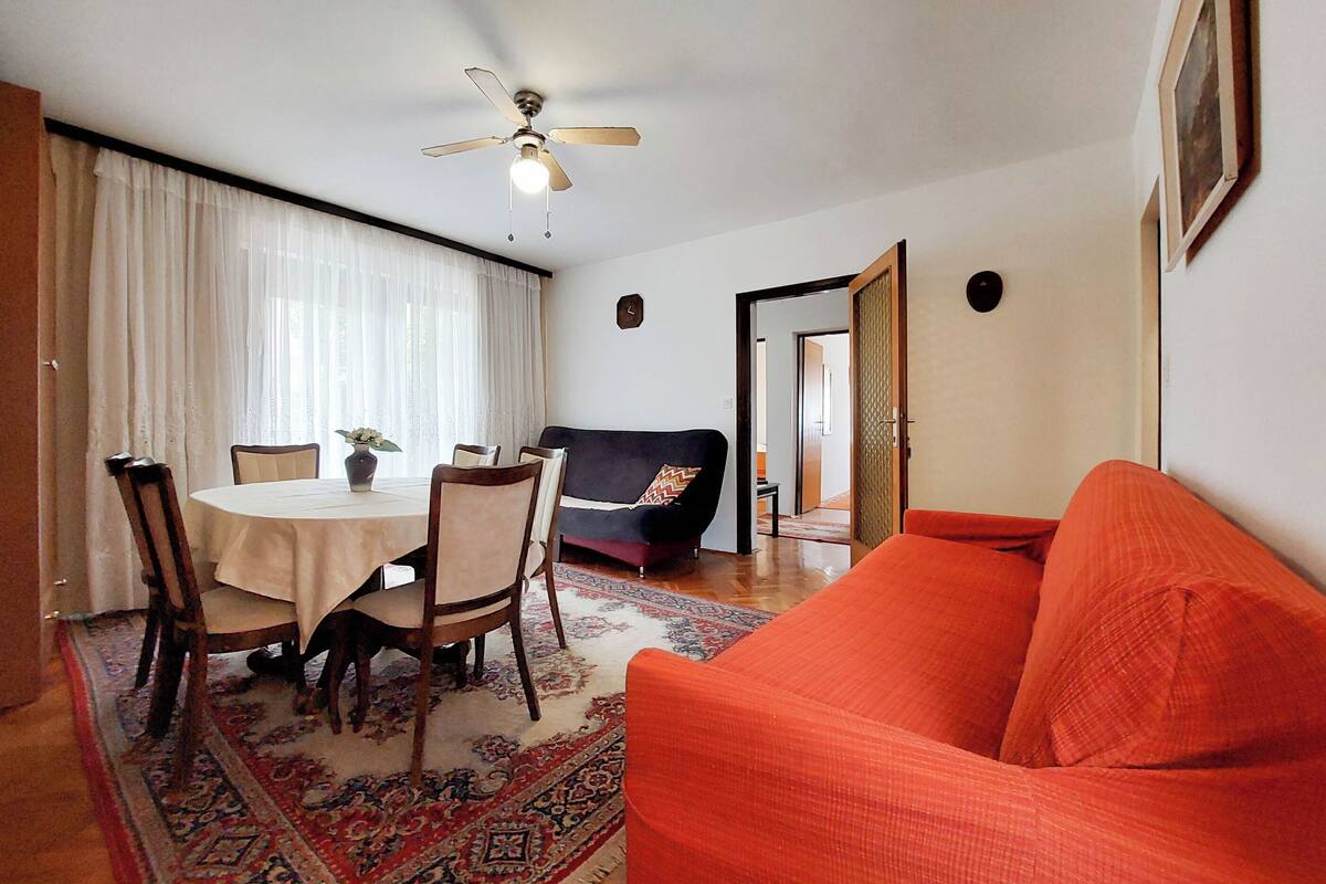 Een woonkamer met een ronde eettafel, stoelen, een bank en een rode slaapbank.