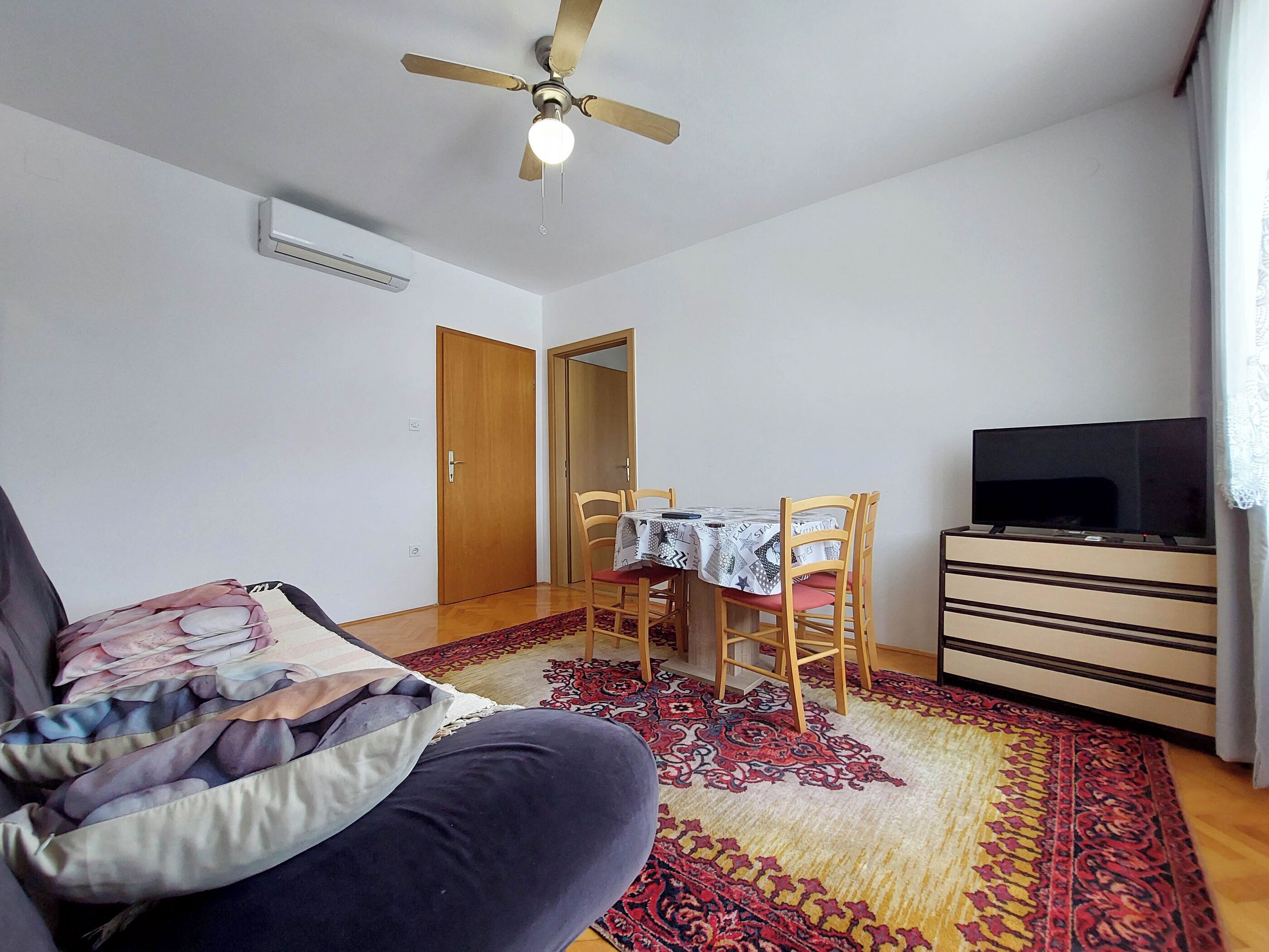 A living room with a sofa, a dining table with chairs, a television, and a ceiling fan.