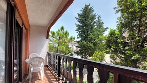 A balcony with a tiled floor, white chairs, and a view of trees and houses. - Apartments Marija (Selce)
