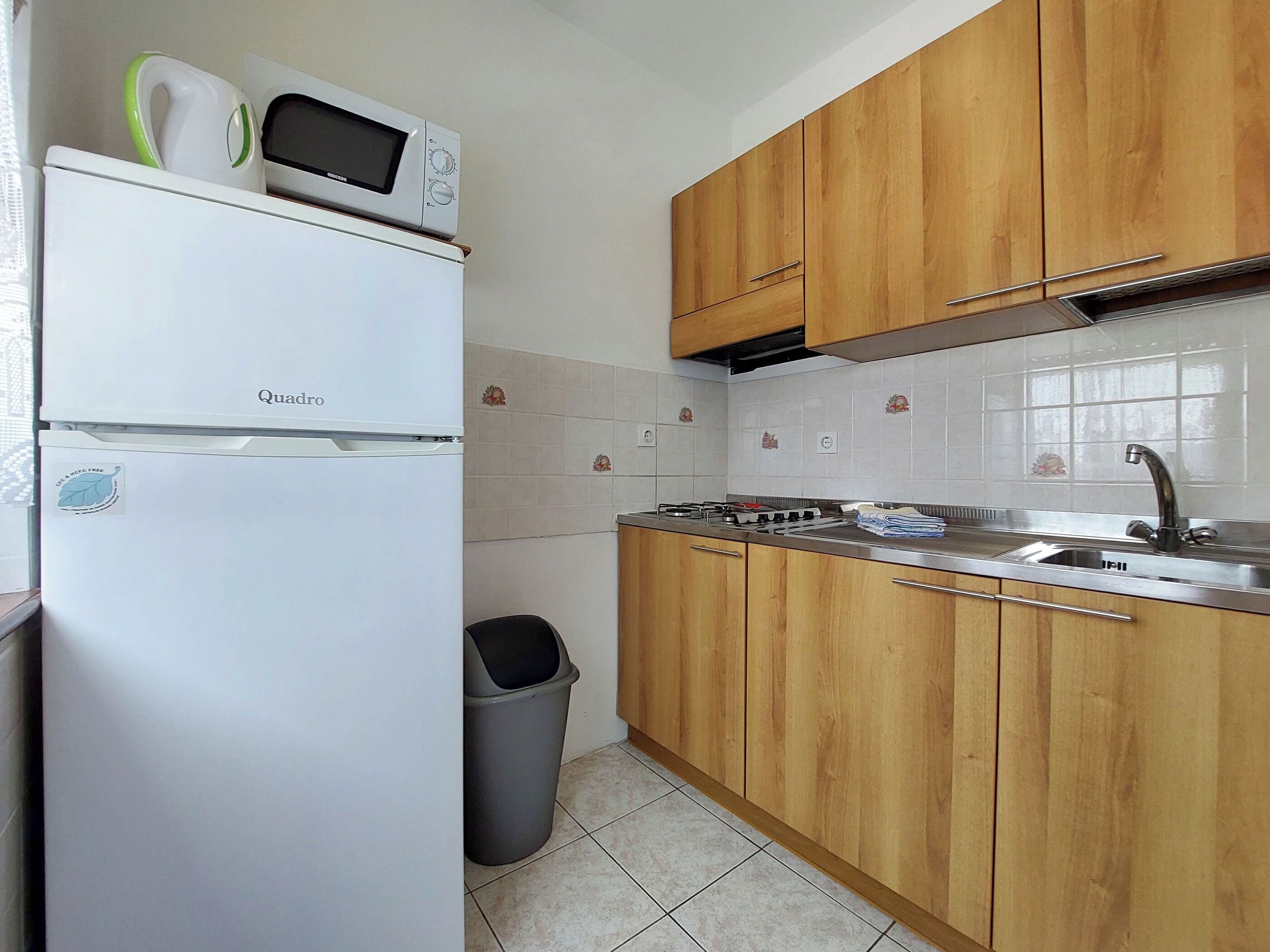 Una cocina compacta con un refrigerador blanco, un microondas, armarios de madera, un lavamanos de acero inoxidable y un salpicadero de azulejos.