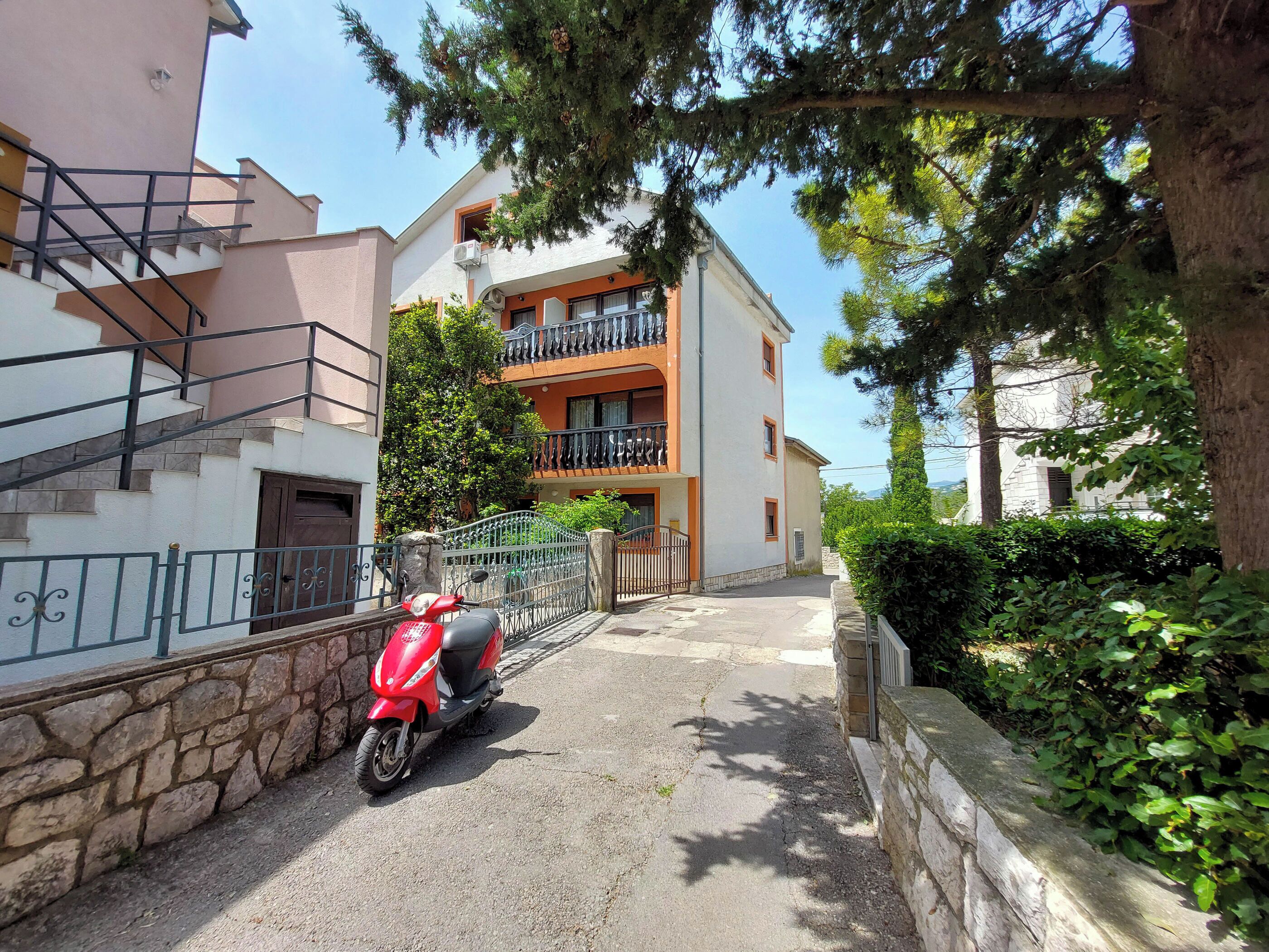 Un immeuble d’habitation devant lequel est garé un scooter rouge.