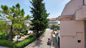 A residential street with a parked scooter, a large tree, and a building with a balcony. - Apartments Marija (Selce)