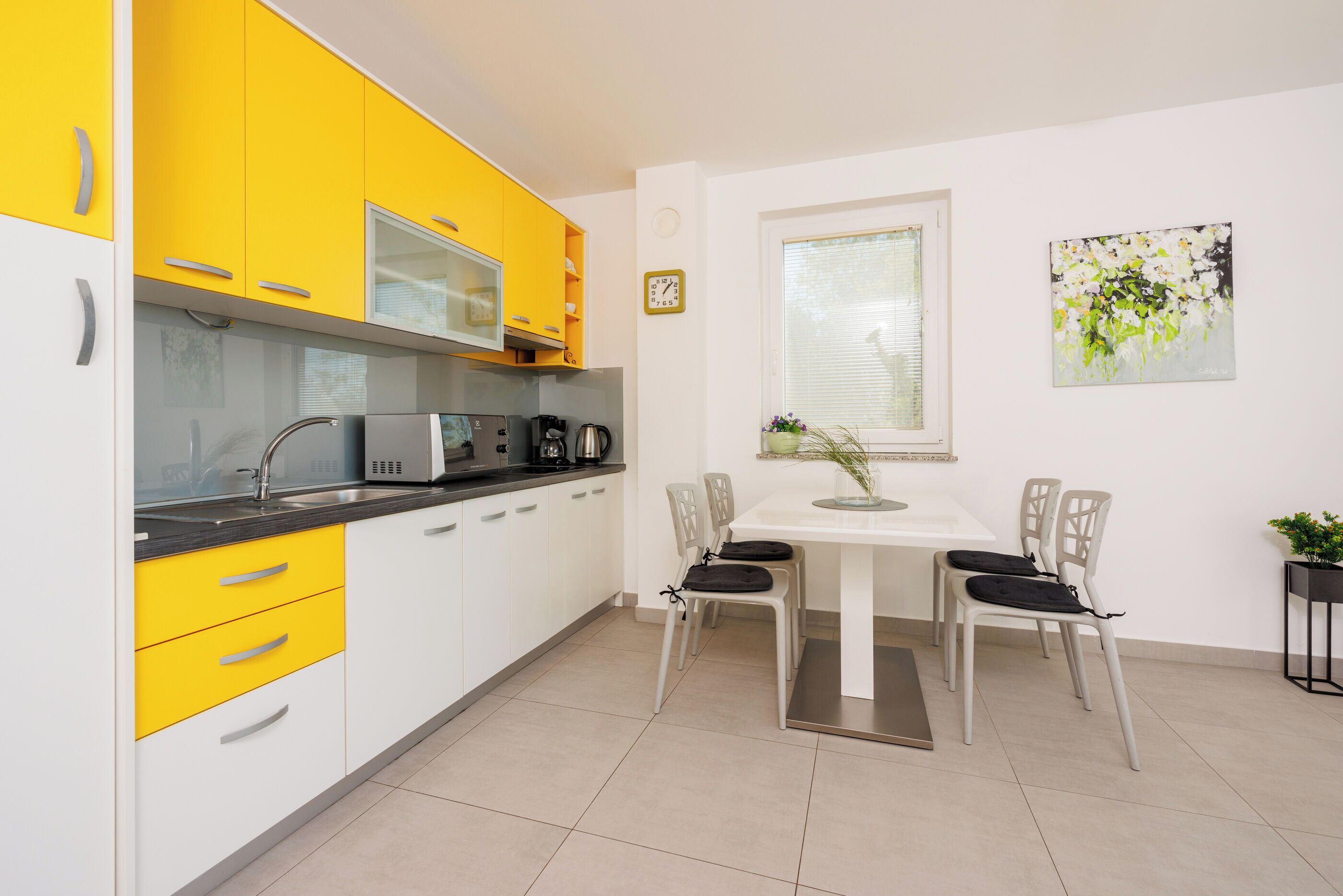 A modern kitchen with yellow cabinets, a white dining table, and two chairs.