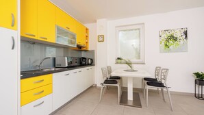 Een moderne keuken met gele kastjes, een witte eettafel en twee stoelen.