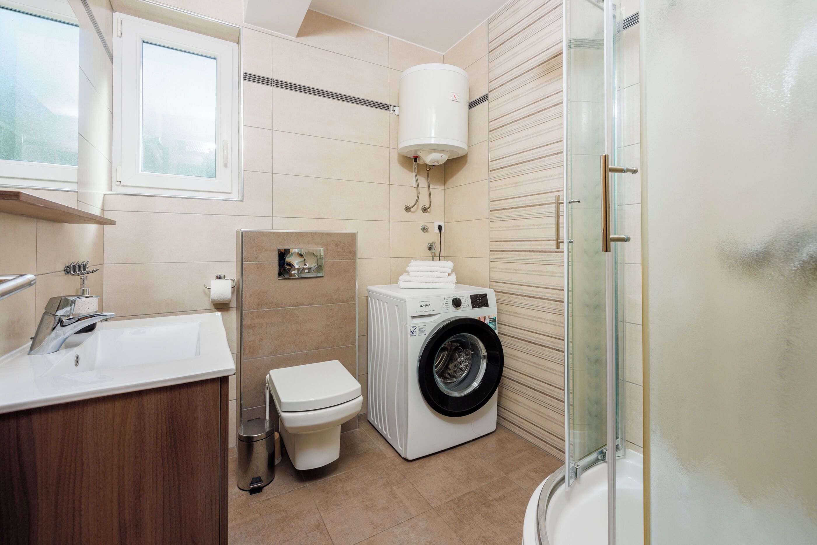 Un baño moderno con lavamanos, inodoro, lavadora y cabina de ducha de vidrio.