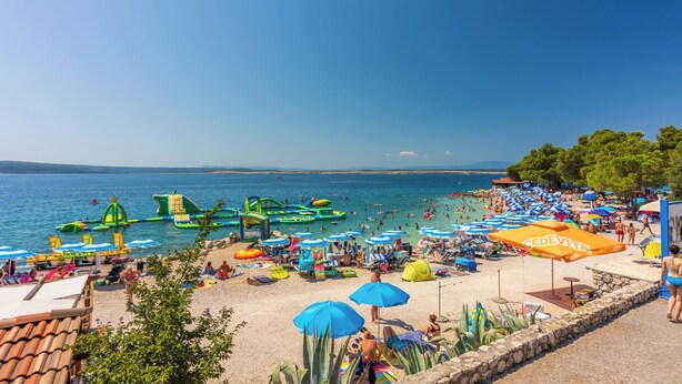 Een strand met parasols, ligbedden en een waterpark.