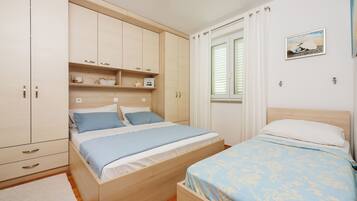 Un dormitorio con dos camas, un armario, una ventana con cortinas y un cuadro colgado en la pared.